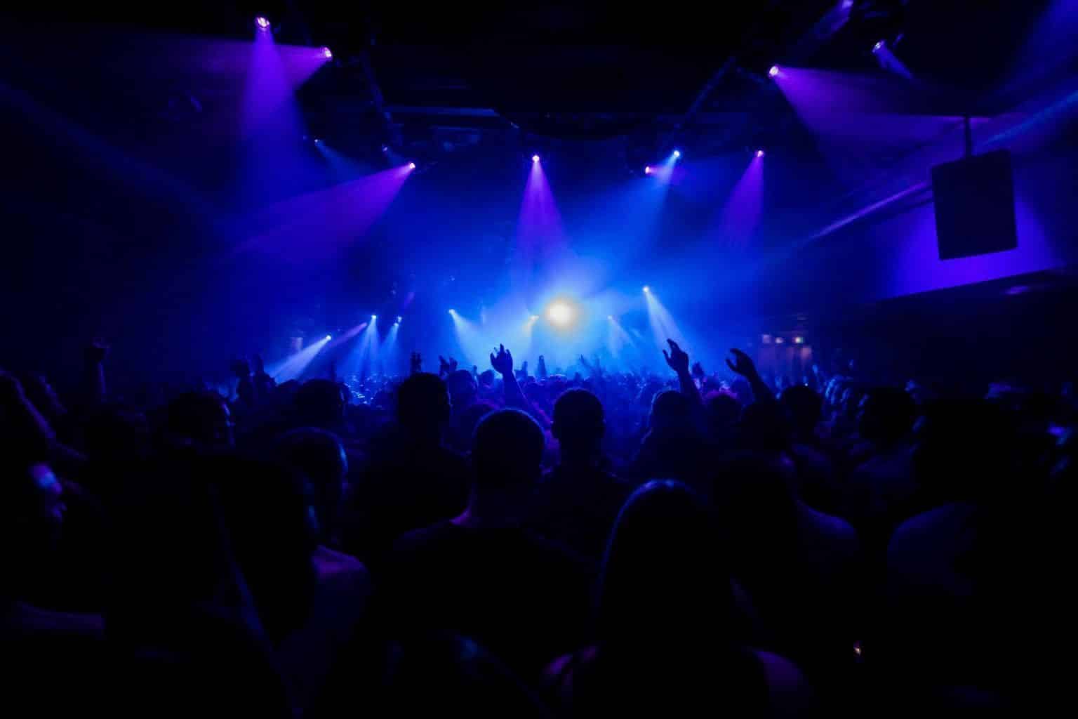 A packed club dance floor under blue and violet lights