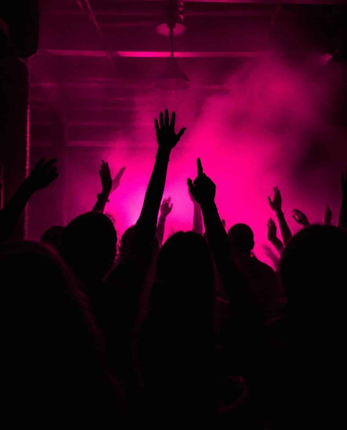 Silhouetted clubbers with arms up against pink backlight and smoke